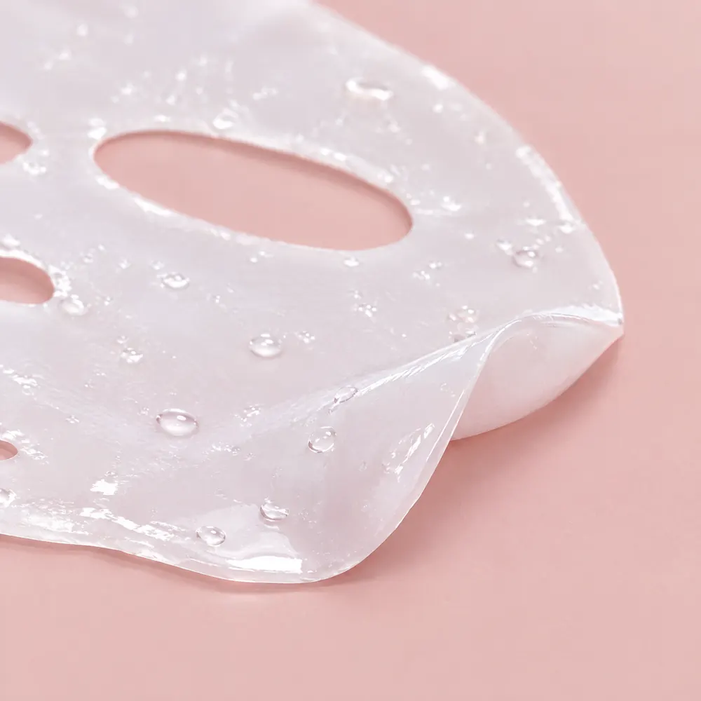 De cerca, la lámina de hidrogel translúcida, con una esquina levantada sobre una superficie rosada y gotas de gel brillantes encima.